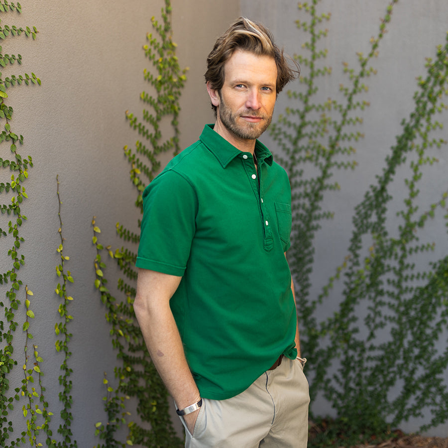 a man standing against a wall wearing a green polo shirt by oobe brand