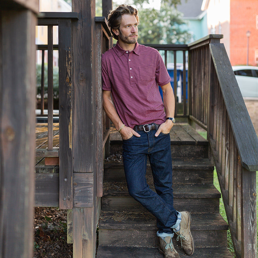 a man leaning on a railing wearing an oobe brand polo shirt and denim jeans